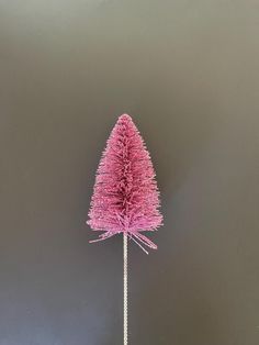 a pink christmas tree on a stick in front of a gray background