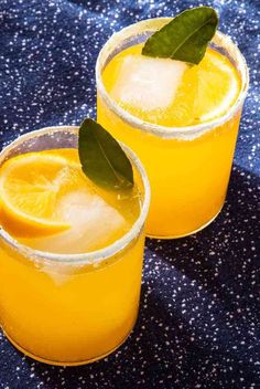 two glasses filled with orange juice and garnished with green leaves on a blue cloth