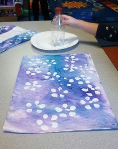 a person is painting on a piece of paper at a table with plates and napkins