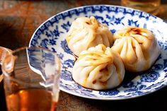 three small dumplings on a blue and white plate next to a glass of tea