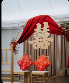 a red and white wedding arch decorated with chinese characters on it's side, surrounded by two gold chairs