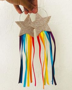 a person is holding two star shaped earrings with rainbow streamers hanging from the side