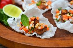 some food is sitting on a wooden platter with lime wedges and tomatoes in the background