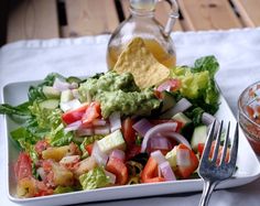 a white plate topped with a salad next to a bowl of salsa and a fork