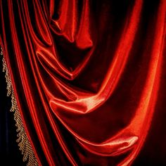 a red velvet curtain with gold trim and lace on the edges is seen in this image