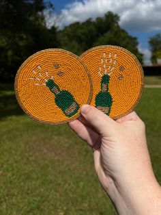 someone is holding up two orange coasters with green bottles on them in the grass