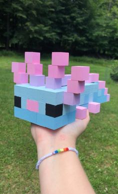 a hand holding up a small block toy in the shape of a cube with pink and blue blocks on it