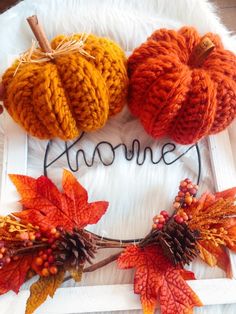 three knitted pumpkins sitting on top of a white frame with the word autumn written in it