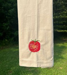 a towel hanging on a clothes line with a red tomato embroidered on the front and side