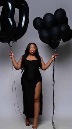 a woman in a black dress is holding some balloons and posing for the camera with her hands behind her back