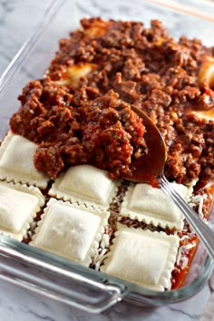 a casserole dish with ravioli and meat sauce being spooned into it