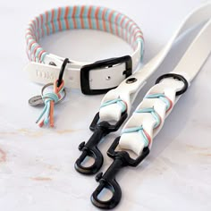 two white leashes with black handles on a marble counter top, one has an orange and blue stripe