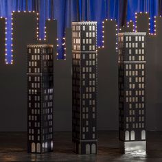 three tall buildings with lights on them in front of a curtained window at night