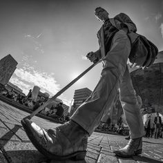 black and white photograph of a man walking on the sidewalk with his cane in hand