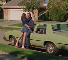 two people are hugging in front of a green car