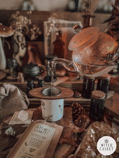 a tea pot pouring water into a cup on top of a table next to other items