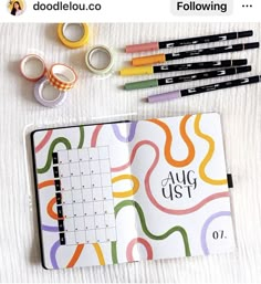 an open planner with markers, tape and pencils next to it on a bed