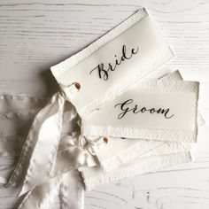 four bride and groom name tags on white fabric with ribbon tied around them, sitting on a wooden surface