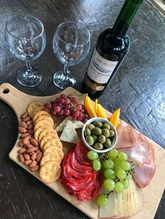 a wine bottle and two glasses on a table with cheese, crackers, olives, grapes and meat