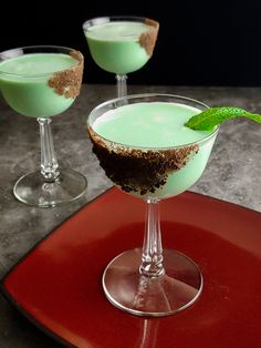 two glasses filled with green liquid on top of a red plate next to each other