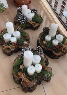 four white candles are placed on wood slices with evergreen and pineconis in the center