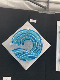 two glass artwork pieces on display at an art show, one is blue and the other is white