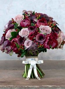 a bouquet of purple and pink flowers in a vase on a wooden table with ribbon around it