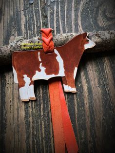 a cow shaped ornament hanging on a wooden wall with red ribbon around it