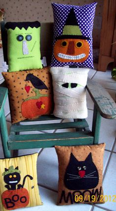 four pillows are sitting on a green chair and one has a black cat, the other is a pumpkin