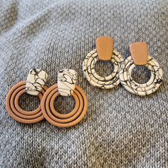 three pairs of wood and marble hoop earrings on a gray blanket with two brown leather ear rings