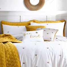 a bed with yellow and white comforters in a bedroom next to a round mirror