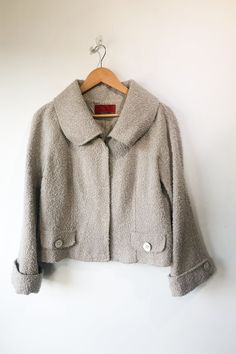 Vintage Carolina Herrera Grey Nubby Wool Jacket. Great condition. Cropped 3/4 sleeve jacket with snap front closure. Has oversized buttons at front faux pockets and cuffs. In allover grey/ivory nubby boucle boiled wool fabric. 54% Acrylic 25% Polyester 19% Wool 2% Nylon. Marked as size 14. Made in Spain. Approx. Measurements: Underarm to Underarm: 20 1/2" Length: 21" Cream Tweed Outerwear With Buttons, Classic Fall Outerwear With 3/4 Sleeve, Tweed Outerwear With Button Cuffs Long Sleeve, Tweed Outerwear With Button Cuffs, Beige 3/4 Sleeve Outerwear For Fall, Spring Tweed Outerwear With Button Cuffs, Boiled Wool Fabric, Boiled Wool, Sleeve Jacket