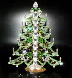 a green and white christmas tree made out of glass beads on a black background with lights