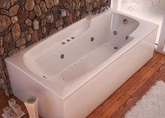 a white bath tub sitting next to a stone wall in a bathroom with wood flooring