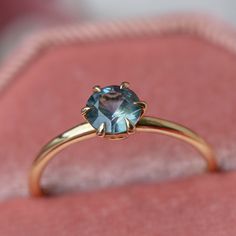 an engagement ring with a blue topazte sits on a pink velvet box