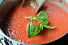 a pot filled with tomato sauce and basil leaves on top of it, being stirred by a wooden spoon