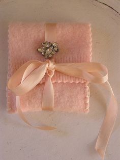 a pink blanket with a bow and brooch sits on a white surface next to a ribbon