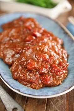 two meat patties covered in tomato sauce on a blue plate next to a fork