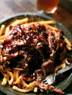 a plate filled with fries and meat covered in barbecue sauce next to a glass of beer