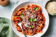 a white bowl filled with pasta and sauce on top of a table next to a wooden spoon