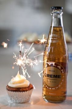 a cupcake next to a bottle of creme on a table with sparklers