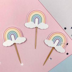 three rainbow lollipop sticks on top of a pink background with stars and clouds