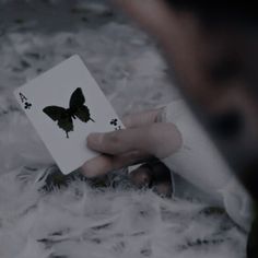 a person holding a playing card with a butterfly on it's back in their left hand