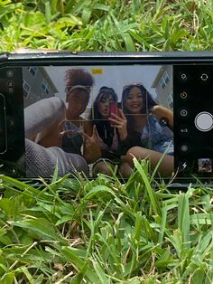 a cell phone laying in the grass with two women taking pictures on it's screen