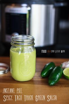 a mason jar filled with green salsa next to some peppers