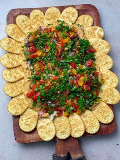 a platter filled with crackers and vegetables on top of a wooden cutting board