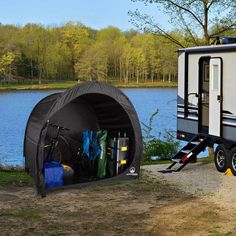 a camper trailer parked next to a lake with its door open and supplies in the back