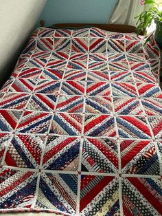 a red, white and blue quilt sitting on top of a bed next to a potted plant