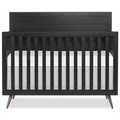 a black crib with white sheets and wood trim on the bottom, in front of a white background