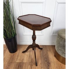 a small wooden table sitting on top of a hard wood floor next to a potted plant